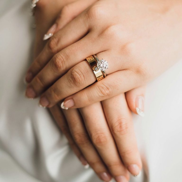 Bodas en Sevilla Manos entrelazadas con anillos de matrimonio y compromiso, uñas decoradas.
